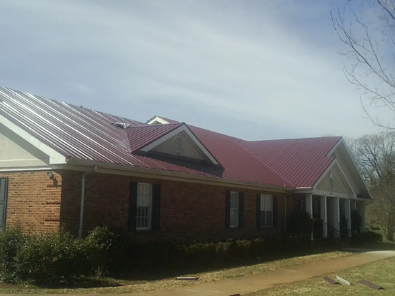 Red metal roof with gabled entries on a long brick building, from a Hail Damage Roof Repair job in Morven