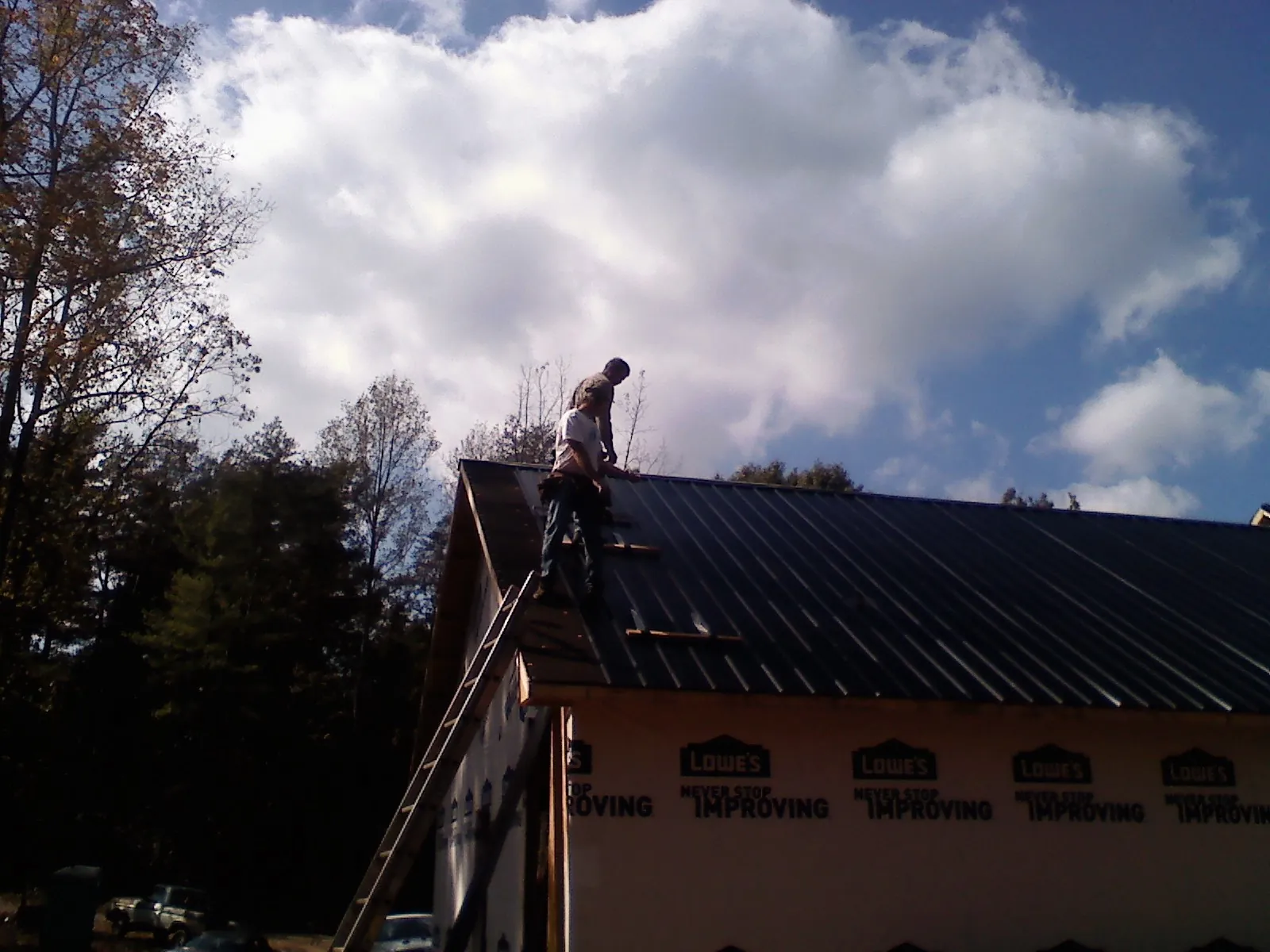 Roofer fastening dark metal panels high against a cloudy sky, from a Roof Inspection job in Morven